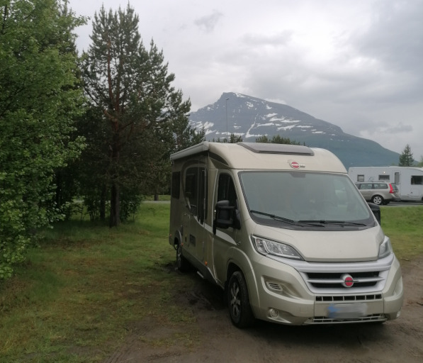 Matkailuauto pysäköitynä. Taustalla vuori ja puita.